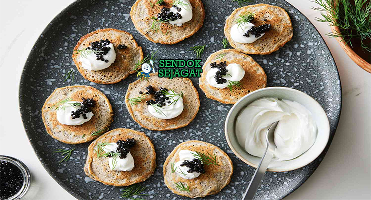 Blini dengan krim asam dan kaviar di piring saji