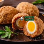 Scotch Egg potong dua telur runny daging renyah di piring saji