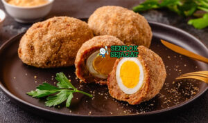 Scotch Egg Juicy Renyah Khas Inggris Scotch Egg potong dua telur runny daging renyah di piring saji