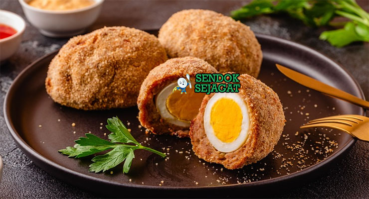 Scotch Egg Juicy Renyah Khas Inggris Scotch Egg potong dua telur runny daging renyah di piring saji