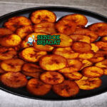 Alloco pisang kepok goreng golden tabur cabe saus tomat pedas di piring anyaman