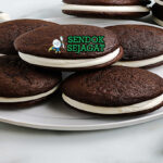 Whoopie Pie cokelat hitam sandwich filling marshmallow putih tebal di atas piring vintage