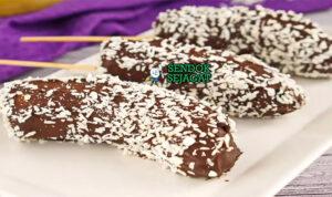 Monkey's Tail Beku Renyah Khas Australia Monkey's Tail pisang beku balur coklat mengkilap tabur kacang almond lemon wedges cherry garnish