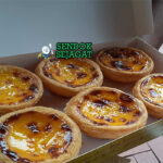 Egg tart Makau asli dengan kulit puff pastry renyah, custard telur kuning lumer, karamel hangus di atas, disajikan di piring putih