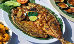 Ikan Bakar Jimbaran Khas Bali – Kulit Mengkilap Manis Gurih Ikan bakar Jimbaran khas Bali kulit mengkilap madu kecap, nasi hangat, lalapan timun kemangi, sambal terasi, piring pantai Jimbaran