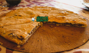 Madfouna roti isi daging Berber panggang golden kecokelatan potong irisan teh mint piring Maroko Sahara Rissani