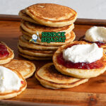 Pikelets khas Australia siap saji: tumpukan mini pancake fluffy keemasan, ditumpuk selai stroberi merah segar dan krim kocok lembut, terlihat menggoda untuk sarapan atau camilan