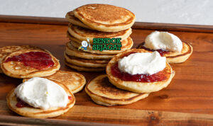 Pikelets khas Australia siap saji: tumpukan mini pancake fluffy keemasan, ditumpuk selai stroberi merah segar dan krim kocok lembut, terlihat menggoda untuk sarapan atau camilan