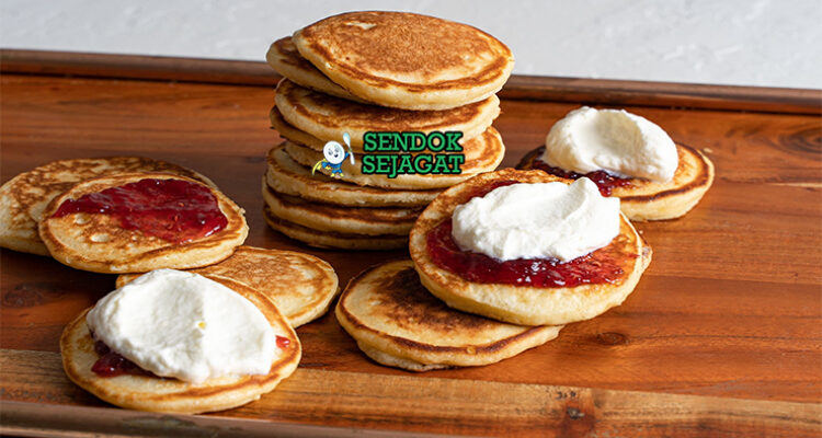 Pikelets khas Australia siap saji: tumpukan mini pancake fluffy keemasan, ditumpuk selai stroberi merah segar dan krim kocok lembut, terlihat menggoda untuk sarapan atau camilan