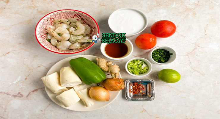 Bahan segar resep bobó de camarão Brasil: udang besar segar, santan kental, ubi kayu potong, tomat merah, bawang bombay, bawang putih, cabai merah, minyak dendê merah, jahe, ketumbar di atas meja dapur kayu