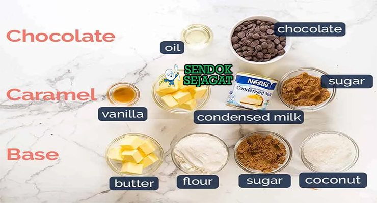 Bahan segar resep caramel slice: tepung terigu, mentega dingin, gula halus, susu kental manis, gula merah, cokelat compound, vanila di atas meja dapur kayu