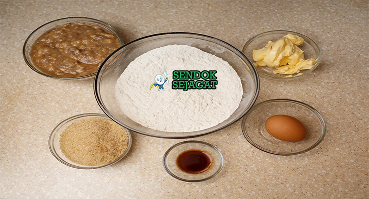 Bahan segar resep Cou-Cou and Flying Fish: tepung jagung kasar, okra hijau segar, fillet flying fish, tomat merah, bawang bombay, bawang putih, cabai, rempah Bajan di atas meja dapur kayu