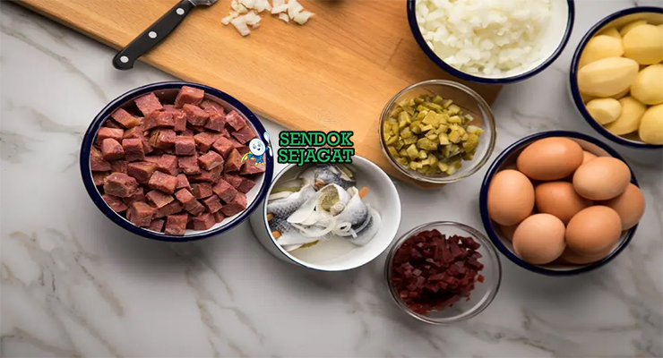 Bahan segar resep labskaus Jerman: kentang potong dadu, daging kornet kaleng, bit merah kaleng, bawang bombay, bawang putih, mentega, susu cair, telur ayam, rollmops herring di atas meja dapur kayu sederhana