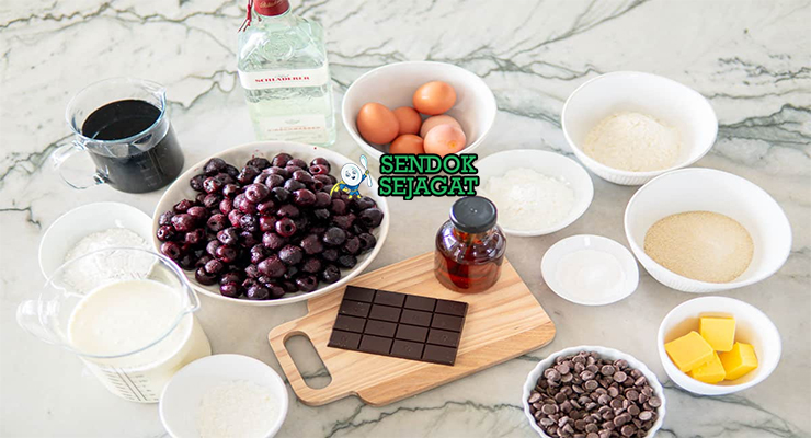 Deretan bahan segar untuk resep Schwarzwälder Kirschtorte: telur, cokelat, ceri kaleng, whipping cream, dan kirschwasser di atas meja dapur