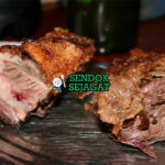 Potongan asado con cuero khas Uruguay dengan kulit renyah keemasan, daging merah muda juicy, disajikan dengan chimichurri hijau segar, chorizo panggang dan kentang al plomo