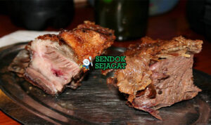 Potongan asado con cuero khas Uruguay dengan kulit renyah keemasan, daging merah muda juicy, disajikan dengan chimichurri hijau segar, chorizo panggang dan kentang al plomo