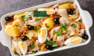 Bacalhau à Gomes de Sá khas Portugal siap saji: loyang berisi ikan kod asin suwir empuk, kentang iris keemasan, bawang karamel, telur rebus potong, zaitun hitam, dan peterseli tabur, terlihat gurih hangat dengan uap mengepul