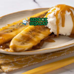 Piring Bananas Foster khas New Orleans dengan pisang karamel flambé, es krim vanila meleleh, dan nyala rum biru, tampak manis dramatis menggugah selera