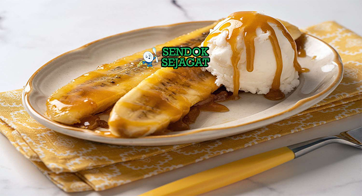 Piring Bananas Foster khas New Orleans dengan pisang karamel flambé, es krim vanila meleleh, dan nyala rum biru, tampak manis dramatis menggugah selera