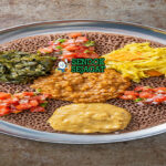 Beyaynetu khas Etiopia siap saji: injera asam ditata berbagai sayur kuah—kik alicha kuning lembut, misir wat merah pedas, gomen hijau gurih, bawang merah iris, dan cabai segar, terlihat penuh warna dan menggoda