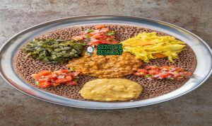 Beyaynetu khas Etiopia siap saji: injera asam ditata berbagai sayur kuah—kik alicha kuning lembut, misir wat merah pedas, gomen hijau gurih, bawang merah iris, dan cabai segar, terlihat penuh warna dan menggoda
