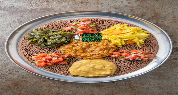 Beyaynetu khas Etiopia siap saji: injera asam ditata berbagai sayur kuah—kik alicha kuning lembut, misir wat merah pedas, gomen hijau gurih, bawang merah iris, dan cabai segar, terlihat penuh warna dan menggoda
