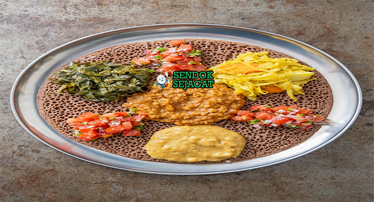 Beyaynetu khas Etiopia siap saji: injera asam ditata berbagai sayur kuah—kik alicha kuning lembut, misir wat merah pedas, gomen hijau gurih, bawang merah iris, dan cabai segar, terlihat penuh warna dan menggoda