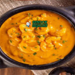 Bobó de camarão khas Brasil siap saji: udang besar juicy dalam kuah santan kental kuning creamy, tomat, bawang, cabai, dan ketumbar segar, terlihat gurih hangat dengan uap mengepul di mangkuk besar