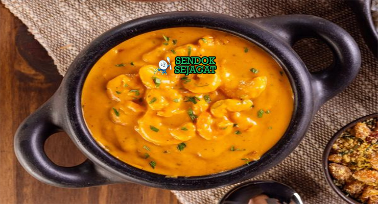 Bobó de camarão khas Brasil siap saji: udang besar juicy dalam kuah santan kental kuning creamy, tomat, bawang, cabai, dan ketumbar segar, terlihat gurih hangat dengan uap mengepul di mangkuk besar