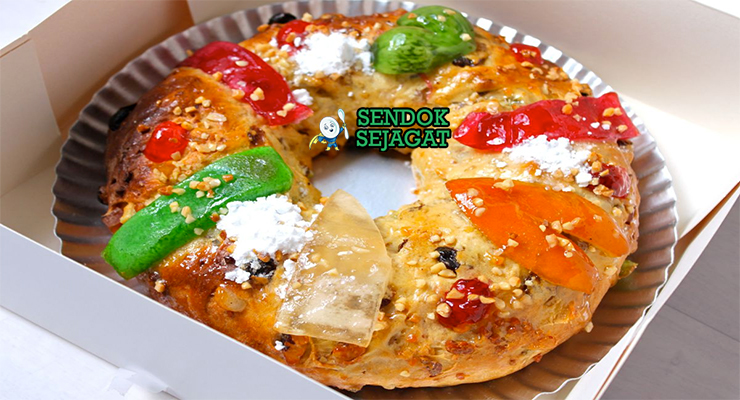 Bolo Rei khas Portugal siap saji: kue roti bundar besar kecokelatan keemasan, tabur almond irisan, gula serbuk halus, penuh kismis dan buah kandir warna-warni, terlihat manis hangat cocok untuk meja Natal