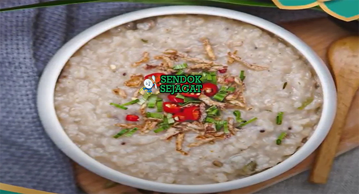 Bubur lambuk khas Malaysia siap saji: bubur beras kental lembut dalam mangkuk besar, tabur bawang goreng renyah, daun bawang iris, seledri, dan limau kasturi peras, terlihat gurih hangat dengan uap mengepul