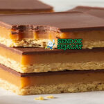 Caramel Slice Potong Sempurna dengan Lapisan Shortbread, Karamel, dan Cokelat Caramel slice khas Australia siap saji: potongan persegi rapi dengan base shortbread renyah, lapisan karamel lembut keemasan, topping cokelat glossy mengkilap, terlihat manis menggoda di piring putih