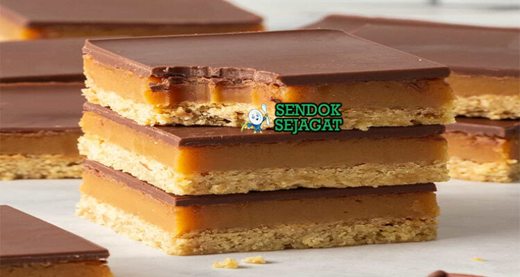 Caramel slice khas Australia siap saji: potongan persegi rapi dengan base shortbread renyah, lapisan karamel lembut keemasan, topping cokelat glossy mengkilap, terlihat manis menggoda di piring putih