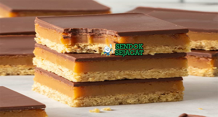 Caramel slice khas Australia siap saji: potongan persegi rapi dengan base shortbread renyah, lapisan karamel lembut keemasan, topping cokelat glossy mengkilap, terlihat manis menggoda di piring putih