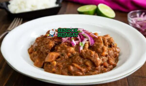 Mangkuk carapulcra khas Peru berisi sup kental kentang kering papa seca, potongan daging babi empuk, kuah merah kecokelatan dari ají panca dan kacang tanah, disajikan dengan nasi putih