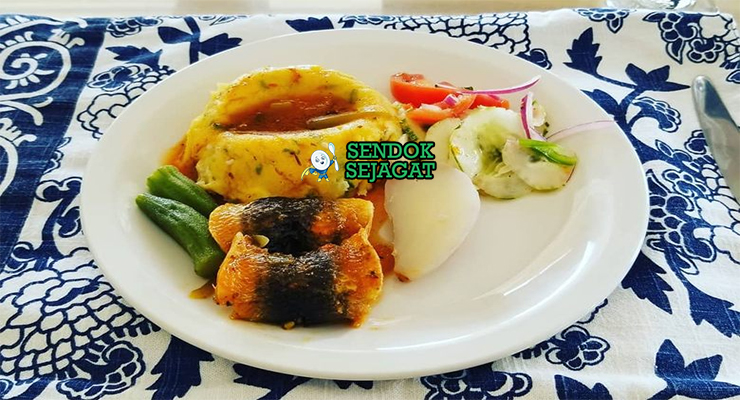 Cou-Cou and Flying Fish khas Barbados siap saji: bubur jagung okra kenyal lembut berbentuk bundar, ditumpuk flying fish goreng renyah keemasan, disiram saus tomat pedas manis, terlihat gurih segar dengan warna cerah tropis