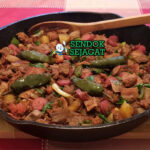 Discada khas Meksiko siap saji: wajan besar berisi tumisan daging sapi, chorizo, bacon, sosis, ayam, paprika merah-hijau, bawang bombay, tomat, cabai, terlihat gurih berapi dengan uap mengepul dan warna cerah