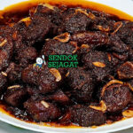 Piring Kala Bhuna khas Bangladesh dengan daging sapi empuk berbalut saus hitam pekat dari bawang karamel, tampak gurih dalam menggugah selera