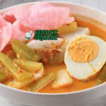 Ketupat sayur khas Betawi siap saji: potongan ketupat pulen dalam mangkuk, disiram kuah santan kuning kental, labu siam empuk, telur rebus, tahu goreng, tauge segar, dan bawang goreng tabur, terlihat gurih hangat dengan uap mengepul