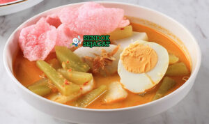 Ketupat sayur khas Betawi siap saji: potongan ketupat pulen dalam mangkuk, disiram kuah santan kuning kental, labu siam empuk, telur rebus, tahu goreng, tauge segar, dan bawang goreng tabur, terlihat gurih hangat dengan uap mengepul