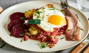 Labskaus khas Jerman utara siap saji: pure kentang lembut kental berwarna krem, daging kornet empuk, bit merah potong dadu, telur mata sapi kuning lumer di atasnya, herring rollmops acar di samping, terlihat gurih hangat menggoda