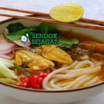 Laksa Medan khas Sumatera Utara siap saji: mangkuk mie kuning kenyal dengan kuah santan kuning kental gurih, ayam suwir lembut, telur rebus, tahu goreng, tauge segar, bawang goreng, dan kerupuk, terlihat menggoda dengan uap hangat