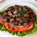 Piring lok lak khas Kamboja dengan potongan daging sapi berbalut saus hitam mengkilap, disajikan bersama selada, tomat, mentimun, bawang bombay dan nasi hangat