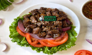 Piring lok lak khas Kamboja dengan potongan daging sapi berbalut saus hitam mengkilap, disajikan bersama selada, tomat, mentimun, bawang bombay dan nasi hangat