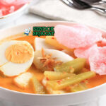 Lontong sayur Medan khas Indonesia siap saji: potongan lontong ketan pulen dalam mangkuk, disiram kuah santan kuning kental, labu siam empuk, telur rebus, tahu goreng, tauge segar, dan bawang goreng tabur, terlihat gurih hangat dengan uap mengepul