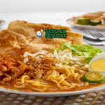 Mee jawa khas Malaysia siap saji: mangkuk mie kuning kenyal dengan kuah kari manis kental berwarna kuning kecokelatan, potongan ayam empuk, telur rebus, tahu goreng, tauge segar, daun bawang iris, dan bawang goreng tabur, terlihat gurih hangat dengan uap mengepul