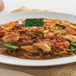 Mie godog khas Jawa siap saji: mangkuk mie kuning kenyal dengan kuah kaldu ayam manis gurih berwarna kecokelatan, ayam suwir lembut, telur rebus, kol iris, sawi hijau, tomat potong, bawang goreng tabur, daun bawang iris, dan kerupuk, terlihat hangat menggoda dengan uap mengepul