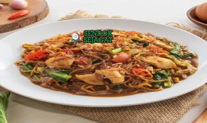 Mie godog khas Jawa siap saji: mangkuk mie kuning kenyal dengan kuah kaldu ayam manis gurih berwarna kecokelatan, ayam suwir lembut, telur rebus, kol iris, sawi hijau, tomat potong, bawang goreng tabur, daun bawang iris, dan kerupuk, terlihat hangat menggoda dengan uap mengepul