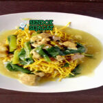 Mie kering khas Makassar siap saji: mie kuning kenyal terbalut bumbu kacang manis gurih berwarna cokelat kental, kikil sapi empuk, bakso urat, tauge segar, telur rebus, bawang goreng tabur, dan kerupuk emping, terlihat menggoda dengan warna cerah