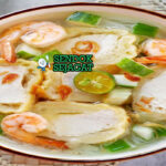 Mangkuk model khas Palembang dengan adonan ikan kenyal isi tahu, disiram kuah kaldu udang bening, taburan seledri, daun bawang, bawang goreng, dan soun